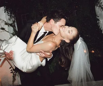 Bride in white gown and veil being affectionately lifted by groom in dark suit during their wedding celebration.