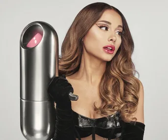 Ariana Grande posing with a large metallic capsule-shaped object, promoting her REM Beauty brand.