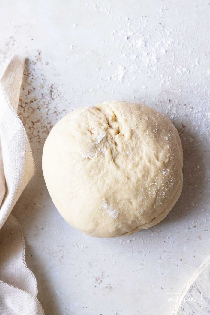 Cinnamon roll dough ball on a lightly dusted white surface.