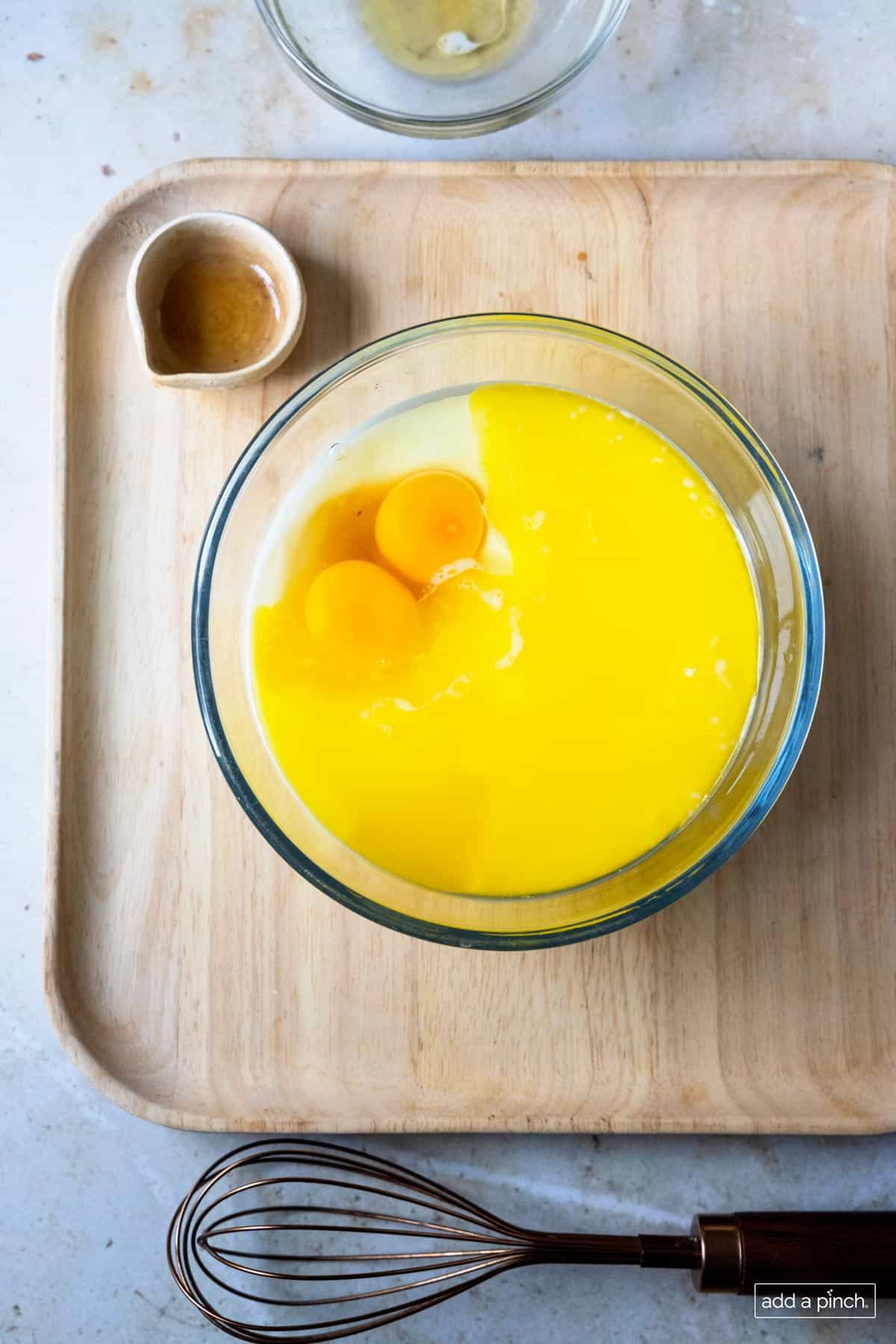 Wet ingredients used to make pancakes in a glass bowl on a wooden board. 