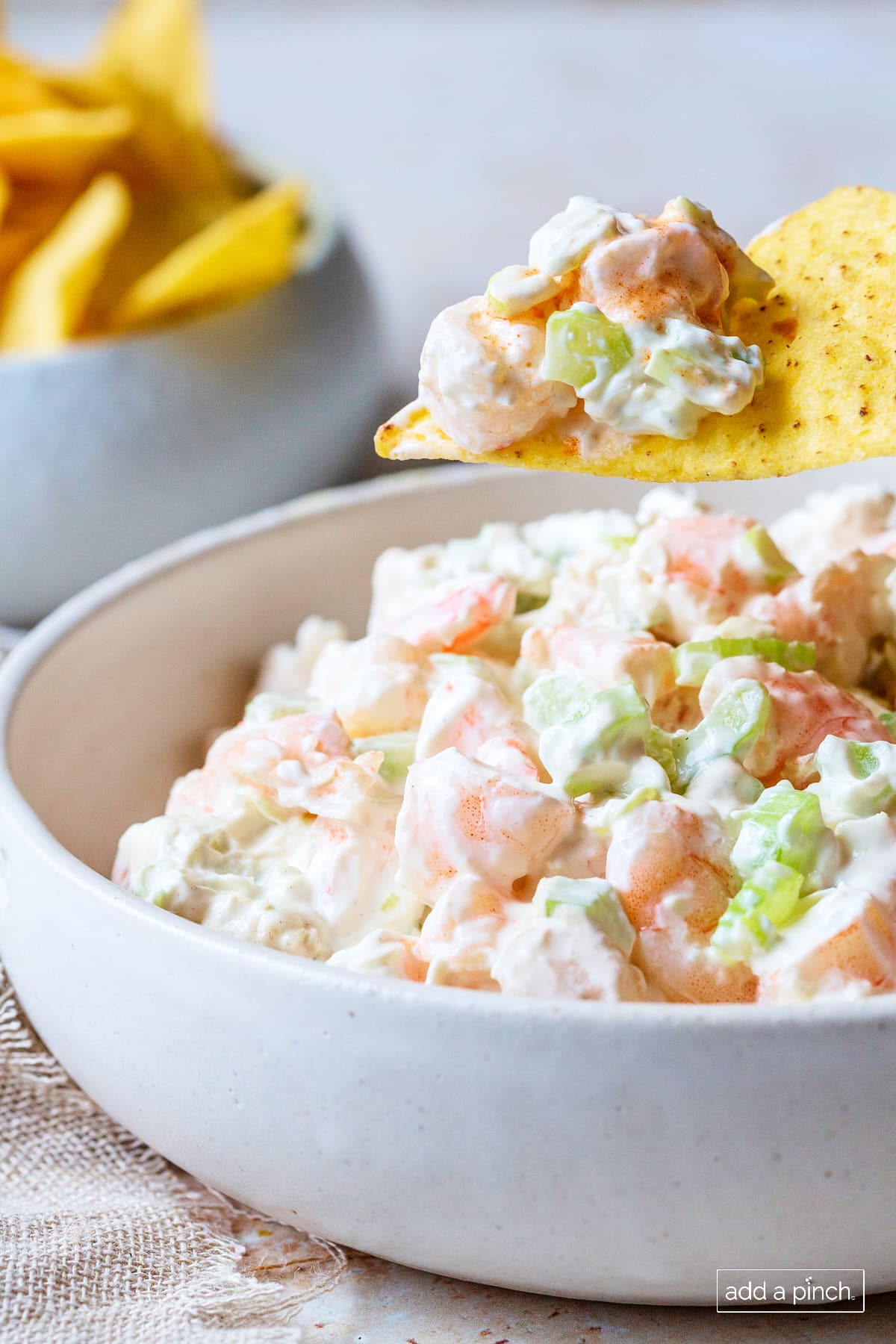 Tortilla chip scoops up a bite of shrimp dip from a white bowl.