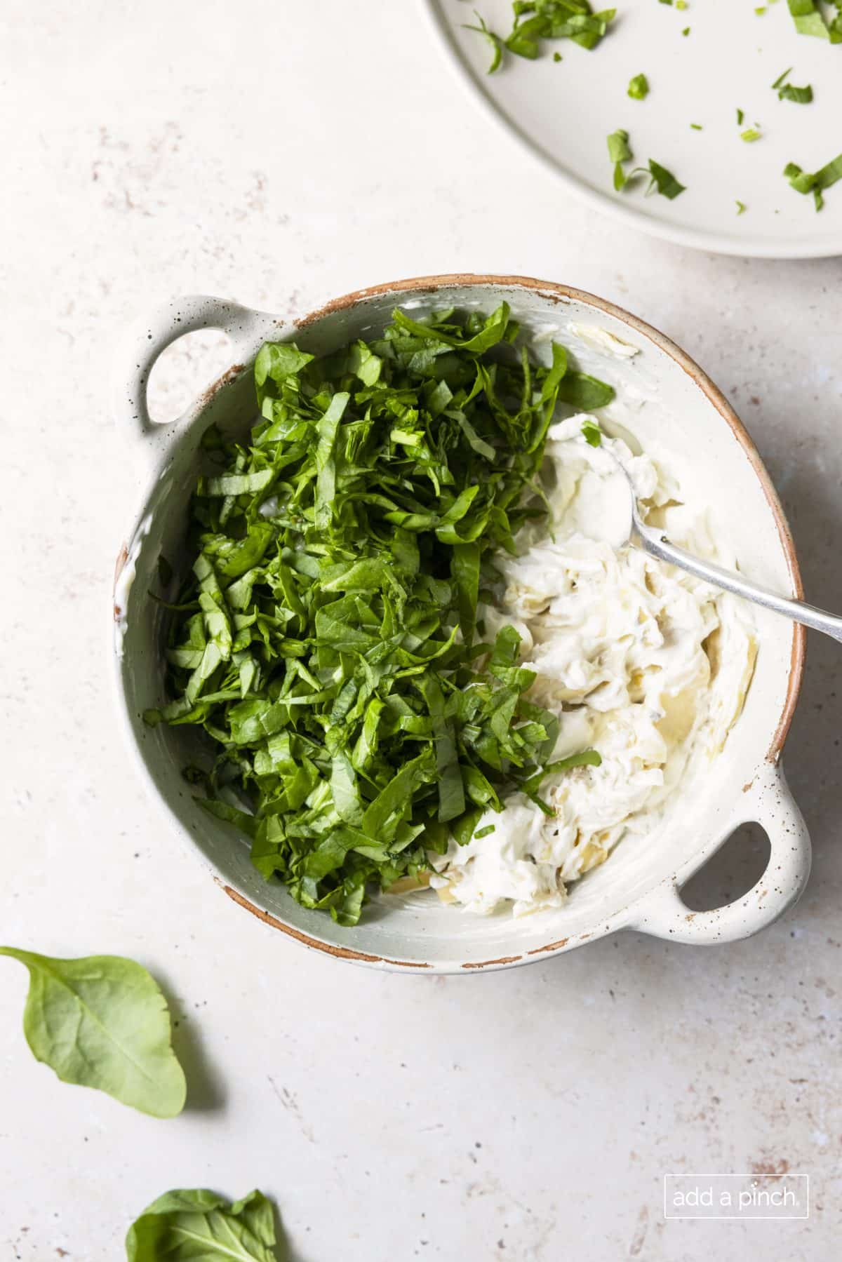 Photo of spinach artichoke dip with fresh spinach added to ingredients in a white baking dish.