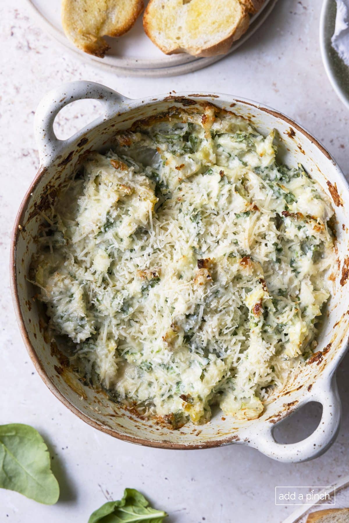 Photograph of baked spinach artichoke dip in a white serving dish.