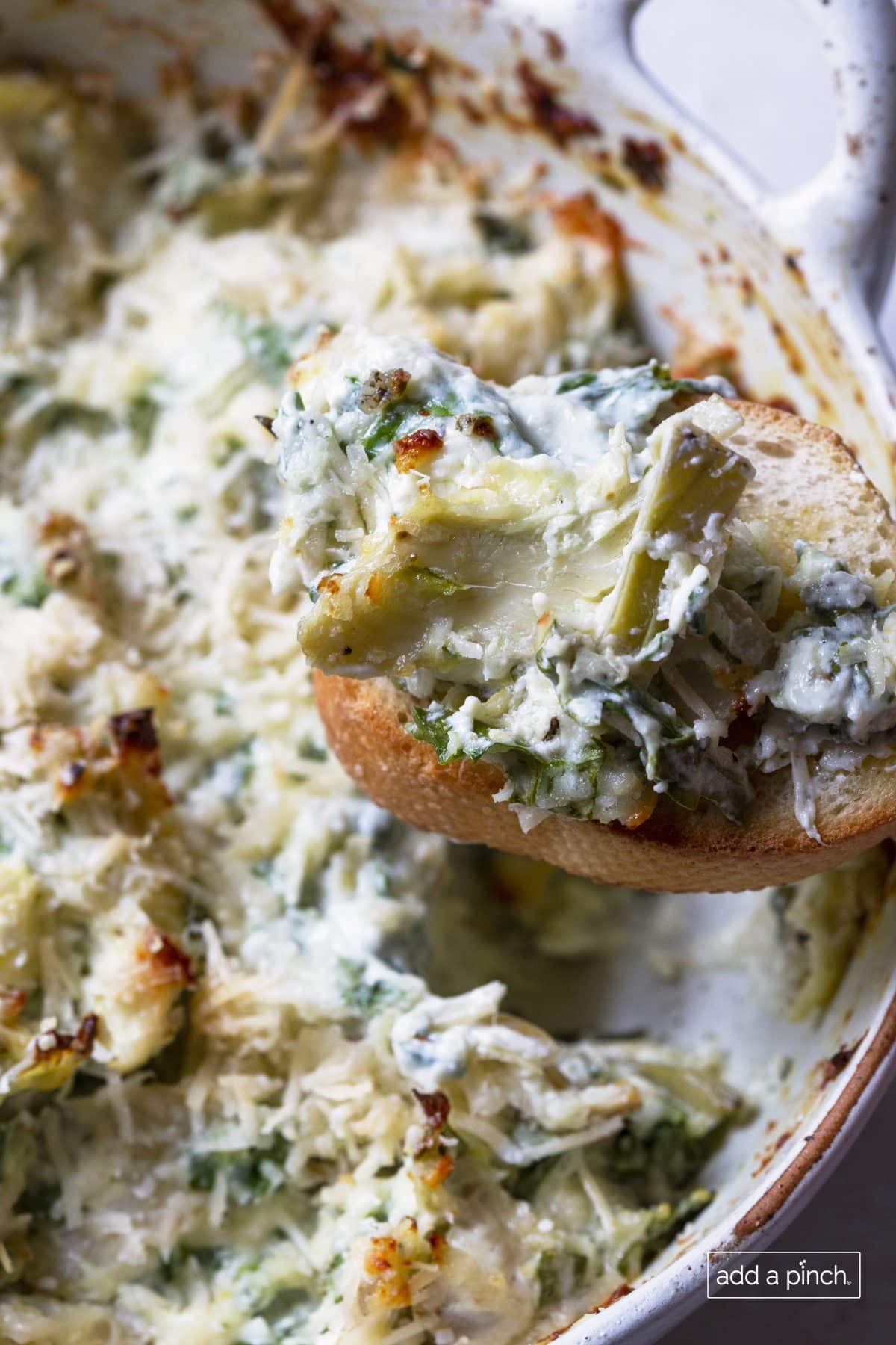 Photo of spinach artichoke dip on a slice of toasted baguette.