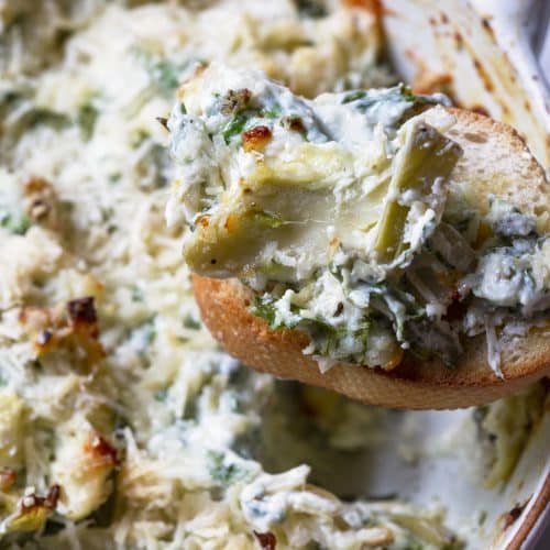 Photo of spinach artichoke dip on a slice of toasted baguette.