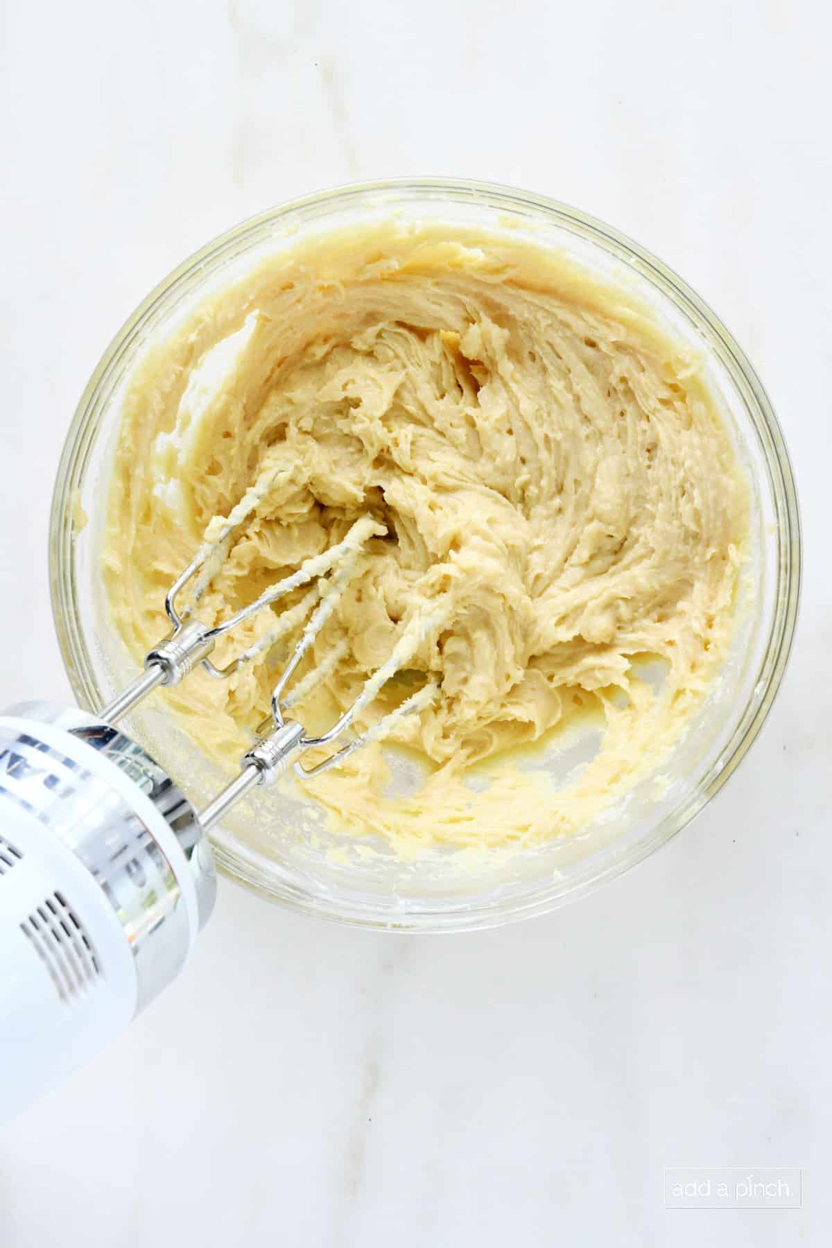 Glass mixing bowl with dip ingredients being blended with a hand mixer. 