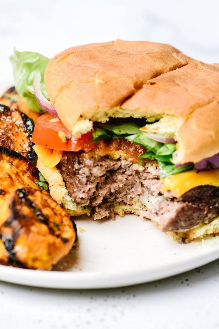 Partially eaten hamburger with bun and all the toppings w grilled sweet potatoes on plate // addapinch.com