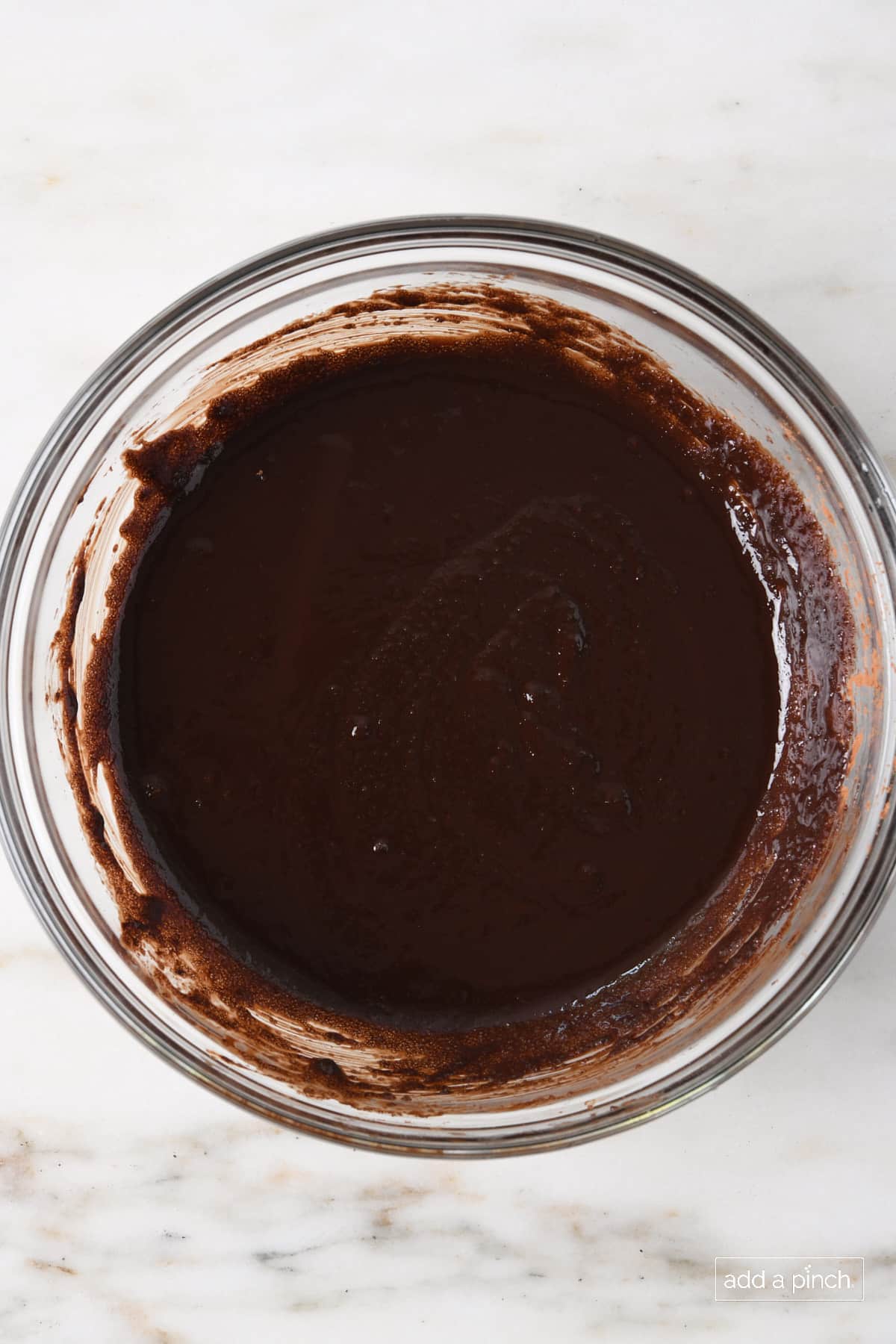 Marble countertop holds glass bowl with brownie batter in it. 