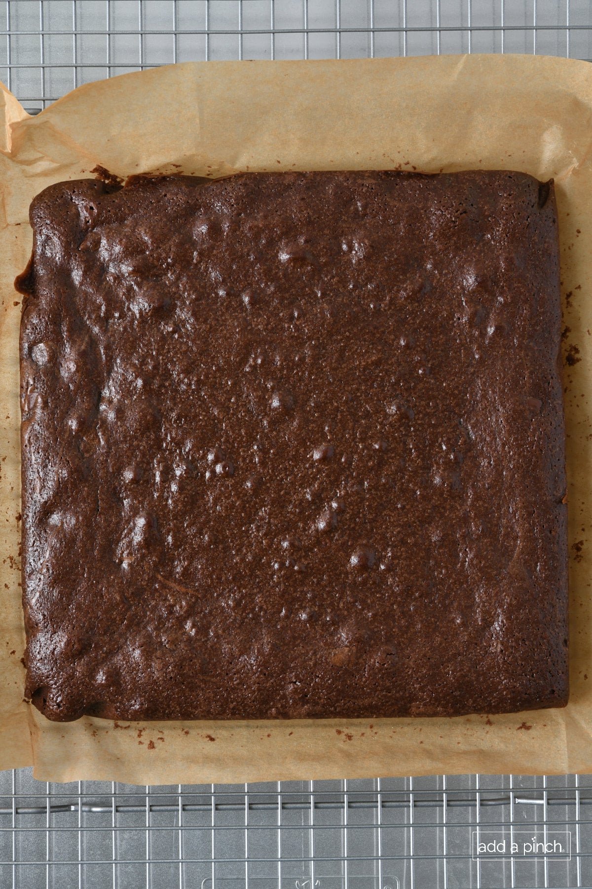 Baked brownie cooling on parchment paper on a wire rack.