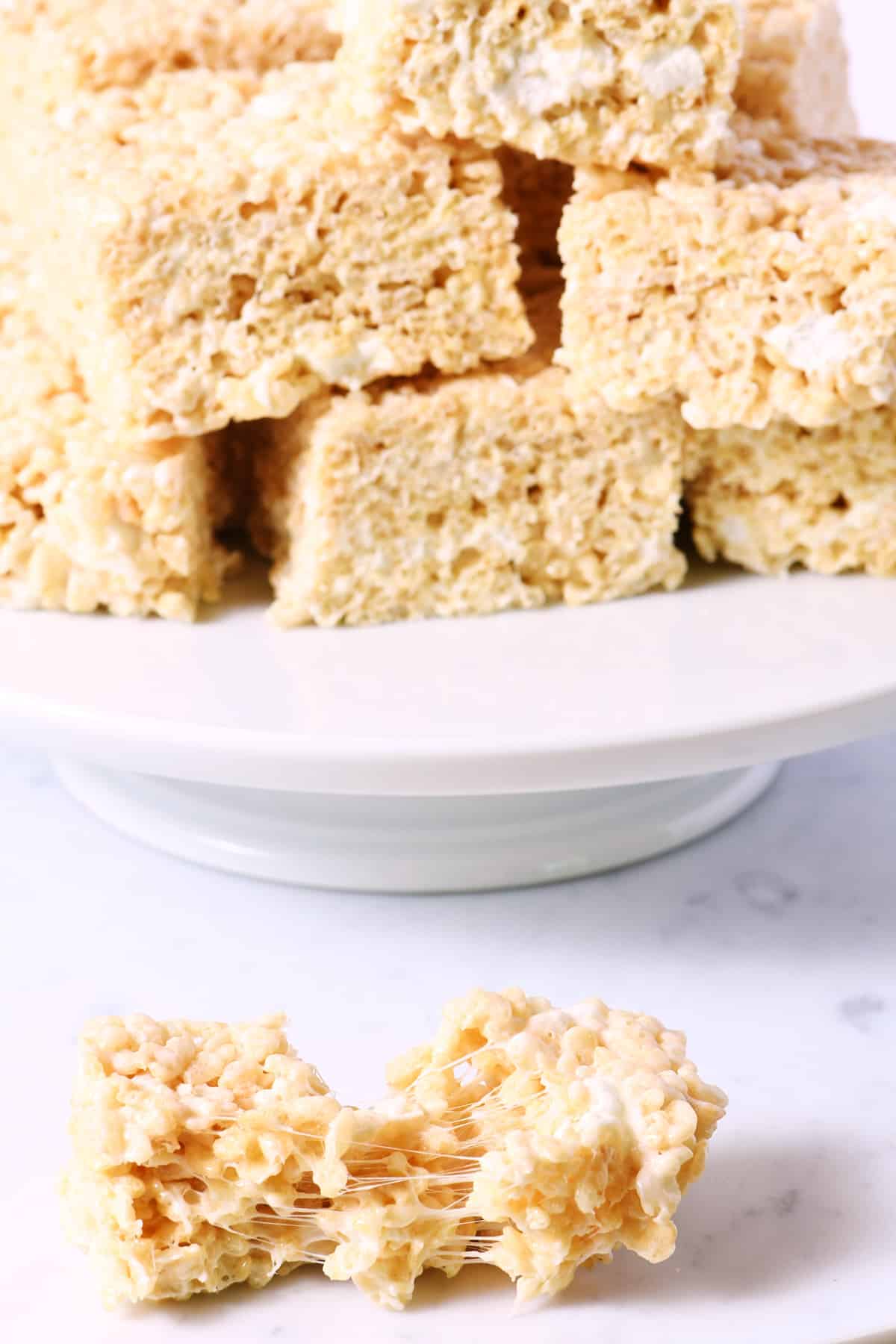 Rice cereal treats on a white bake plate with one in front.