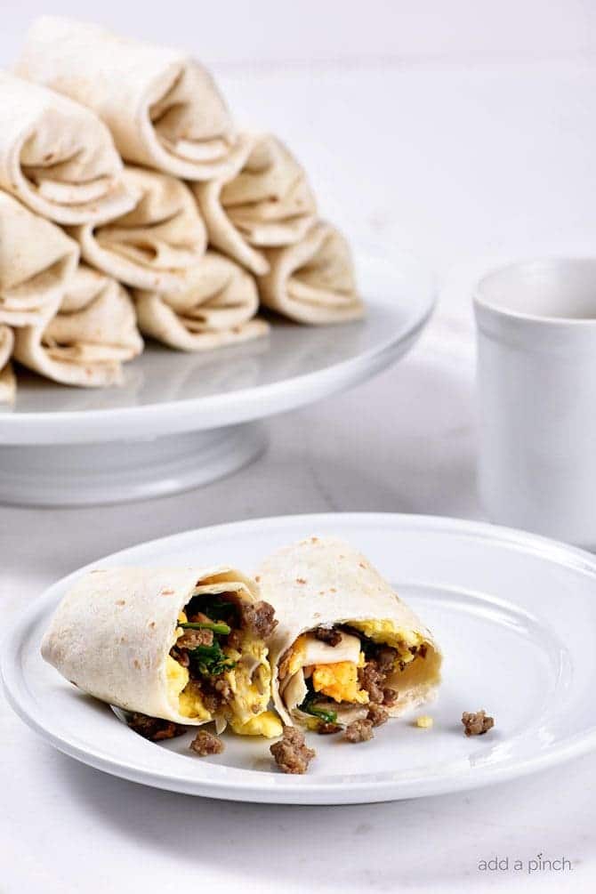 Breakfast burrito on a white plate with stack in the background.