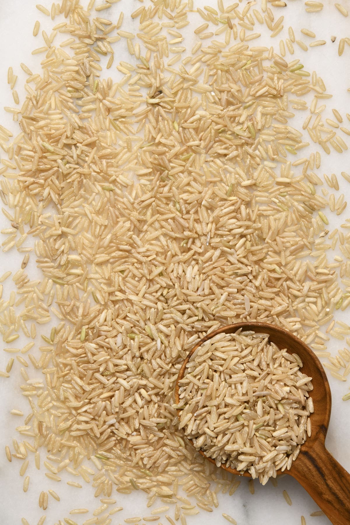 Rice on top of a marble surface with a  wooden scoop.