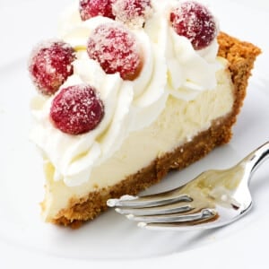 A slice of cheesecake pie topped with whipped cream and sugared cranberries on a white plate.