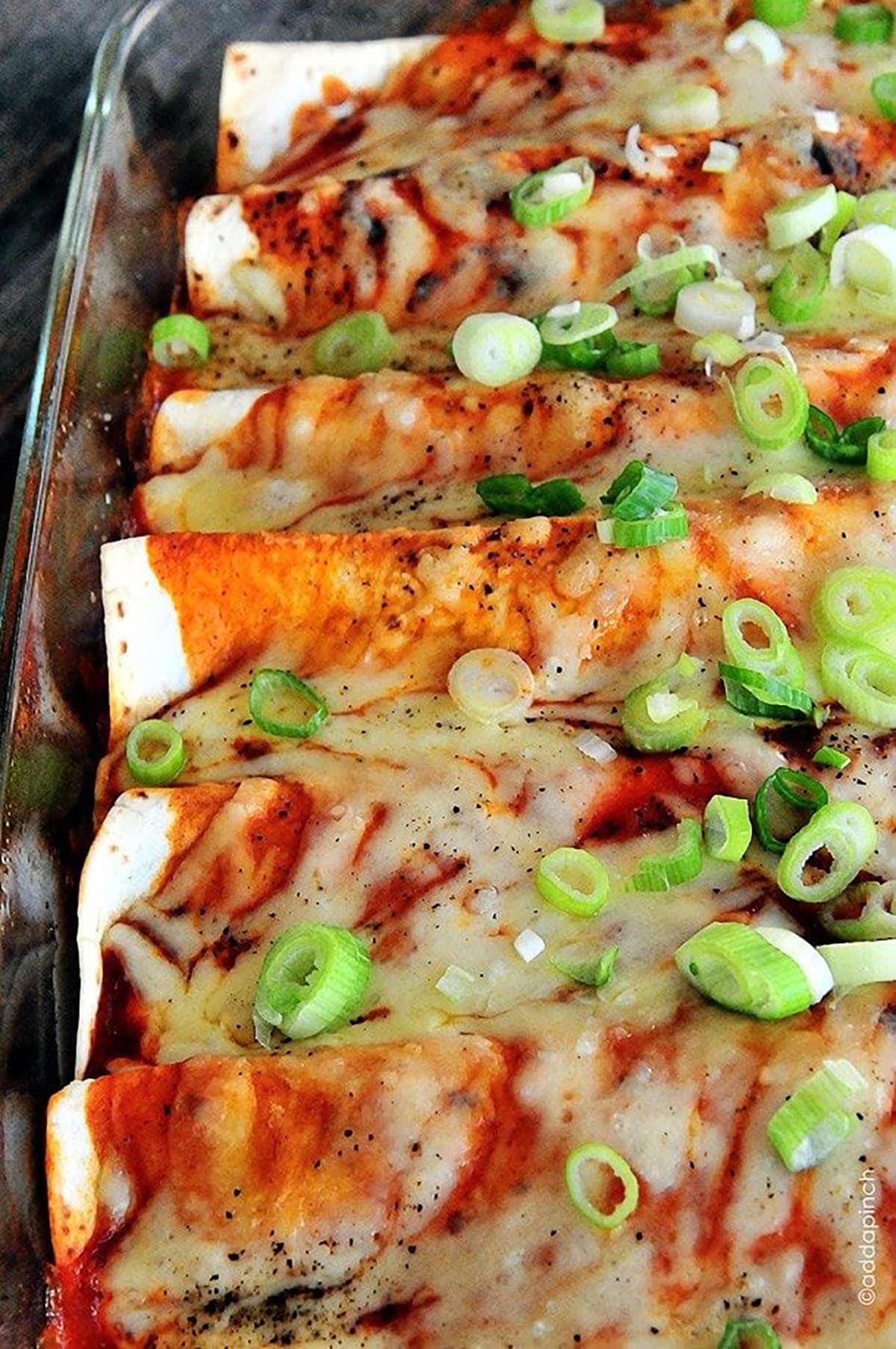 Glass baking dish filled with enchiladas topped with melted cheese and enchilada sauce and garnished with green onion. 