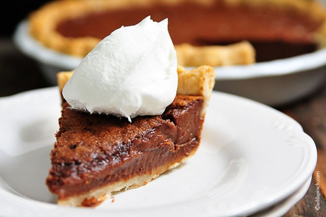 Horizontal photograph of chocolate chess pie on a stack of white dessert plates with full pie in the background. // addapinch.com