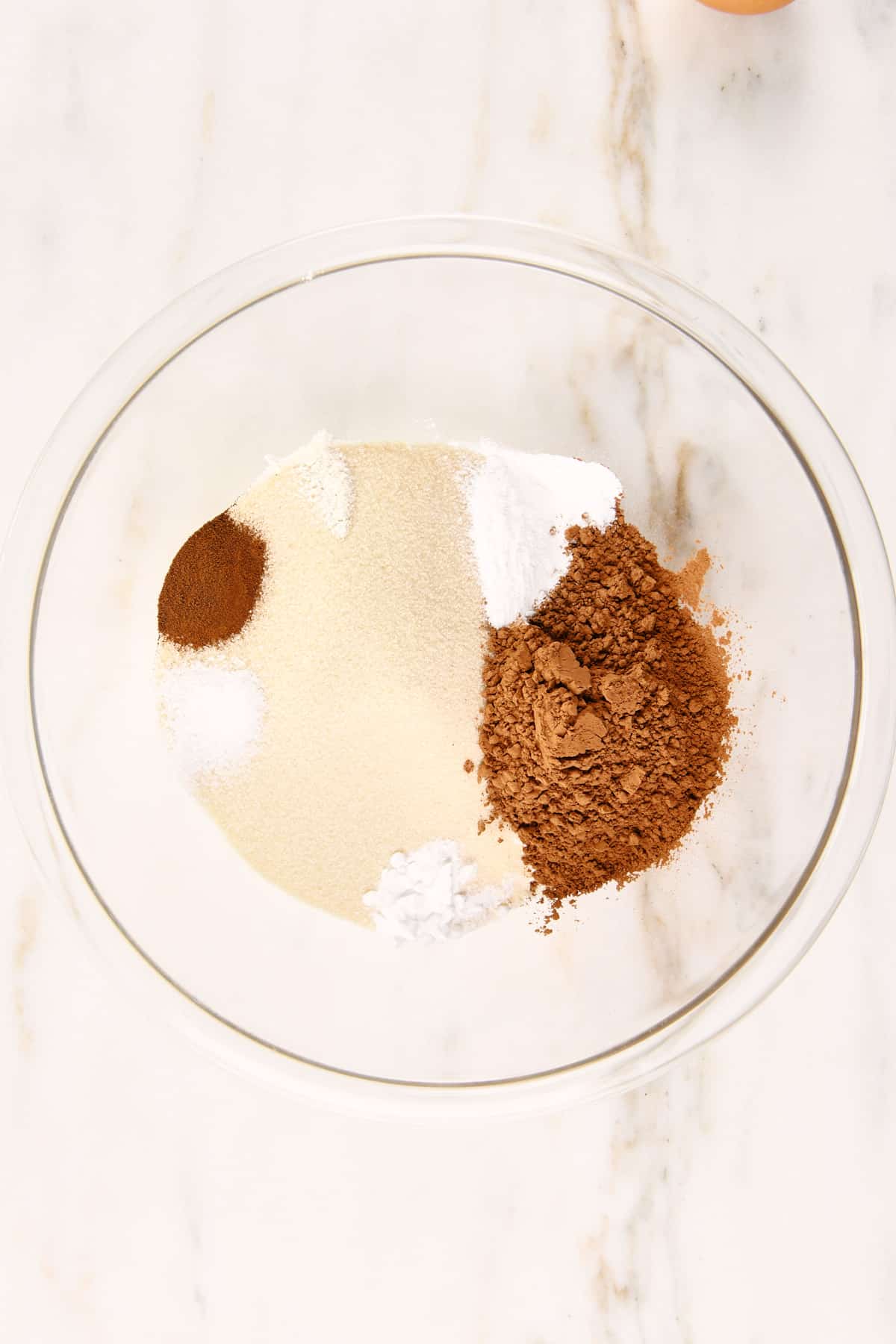 Dry ingredients for a chocolate cake in a glass mixing bowl.