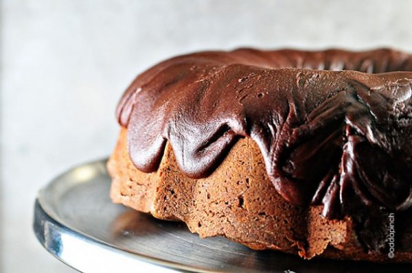 Chocolate pound cake with fudge icing on a silver cake stand.