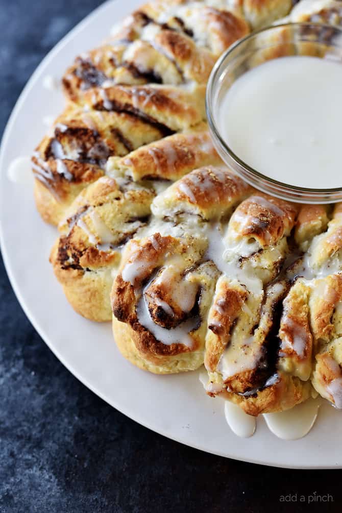 Side view of Cinnamon Roll Wreath with icing drizzled and glaze in bowl in the center of wreath.