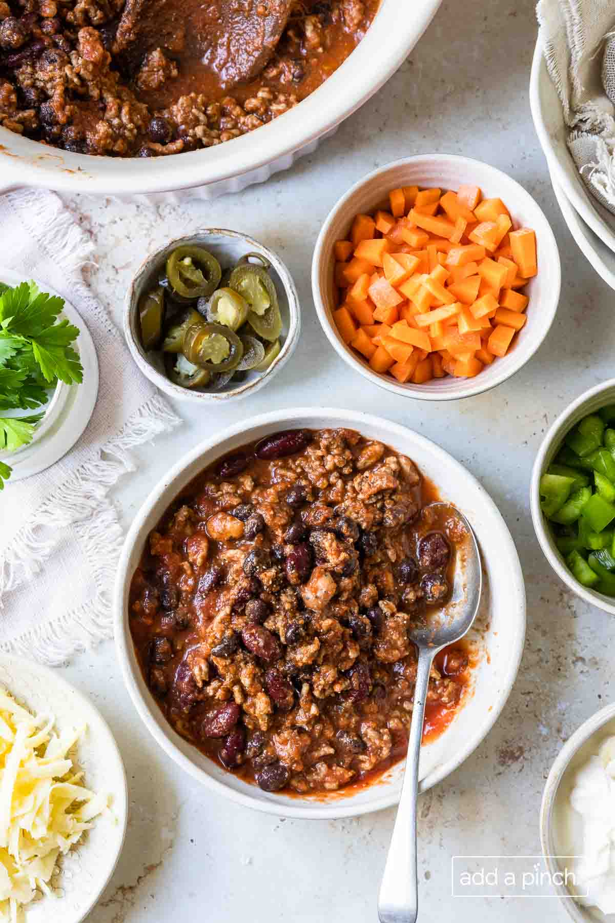 Bowl of chili, surrounded by bowls of optional ingredients and toppings. 
