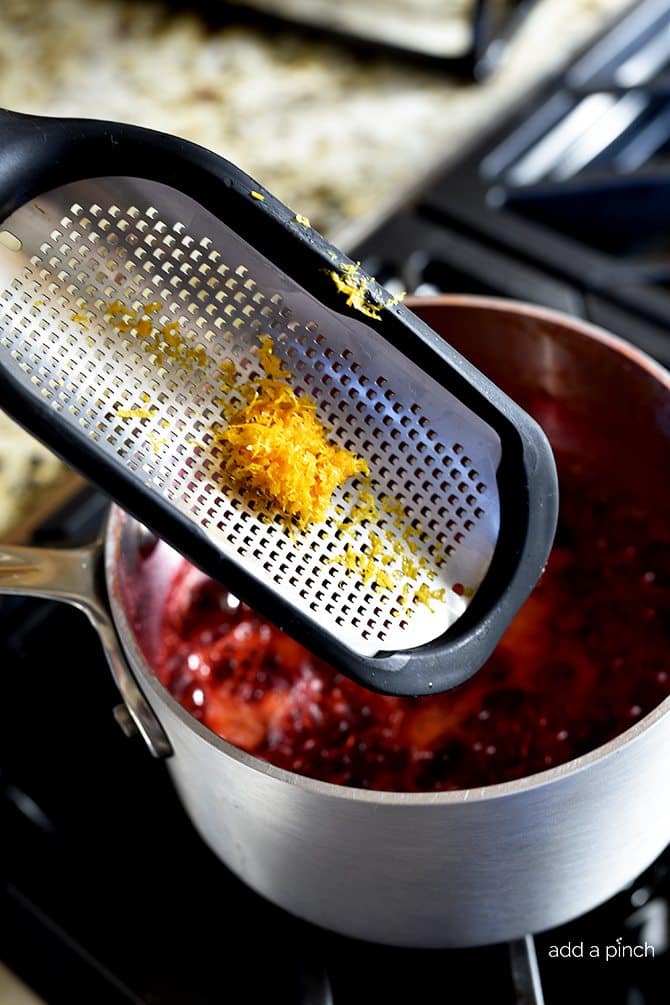 Metal grater with orange zest over saucepan on the stove.