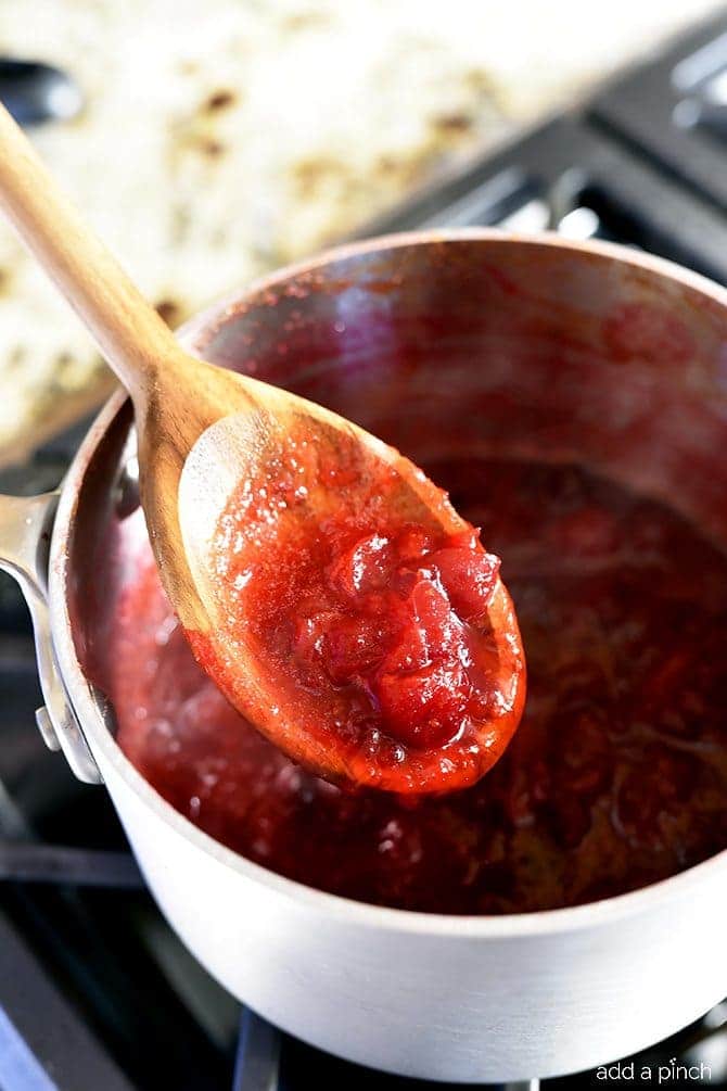 Testing consistency and thickness of cooked Cranberry Sauce with a wooden spoon.