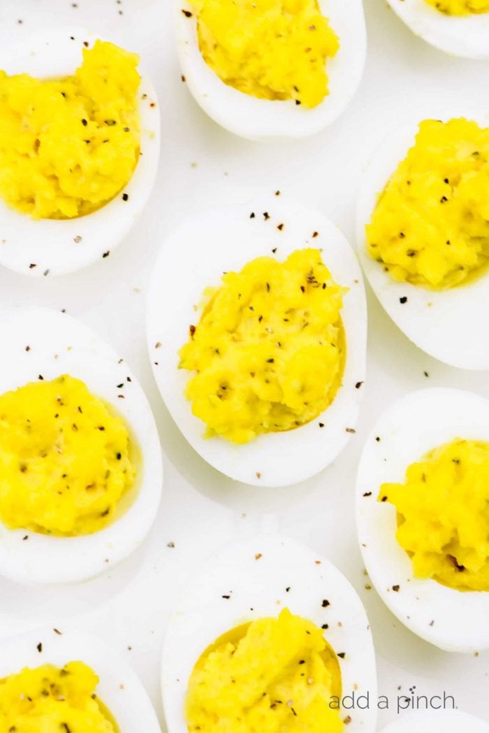Closeup photograph of deviled eggs sprinkled with black pepper on a white platter. 