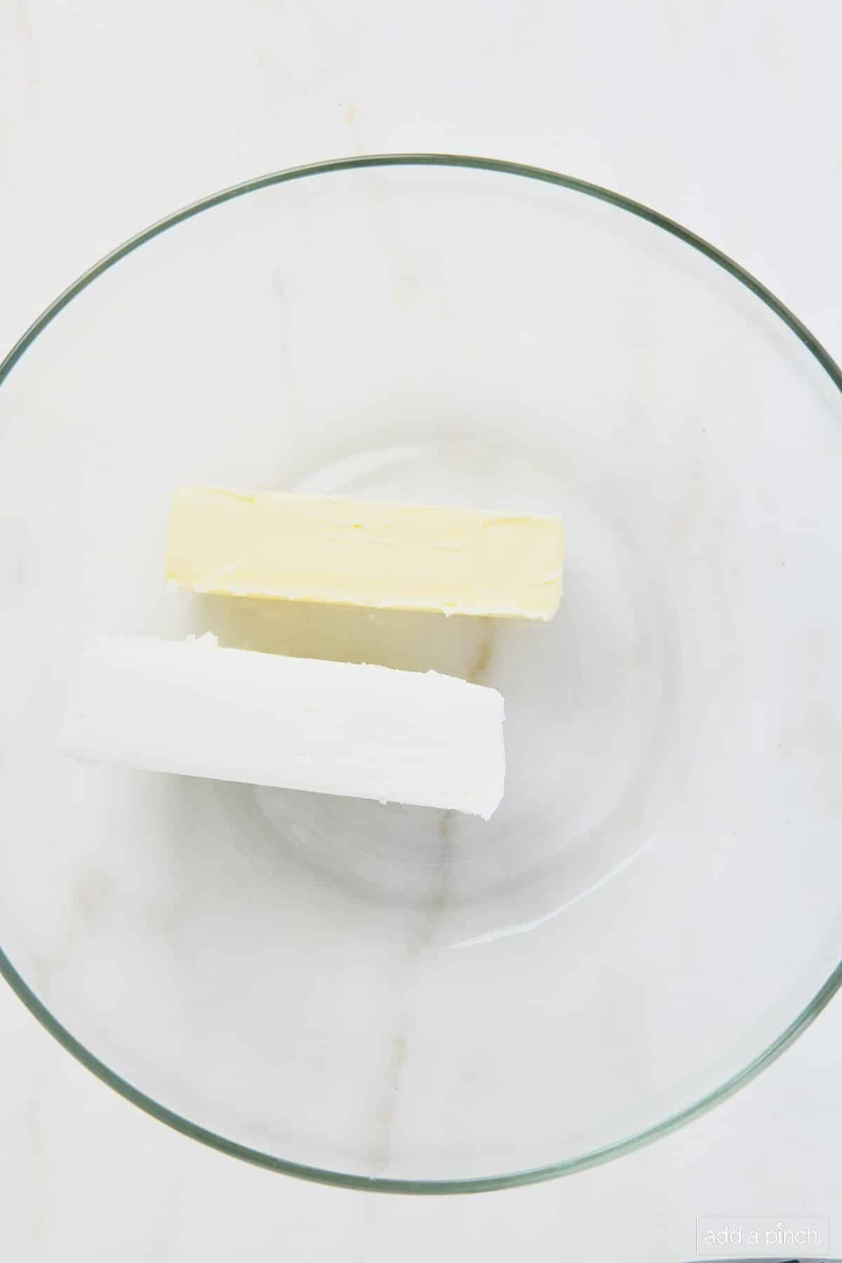 Softened butter and vegetable shortening ready to be creamed together in a glass mixing bowl.