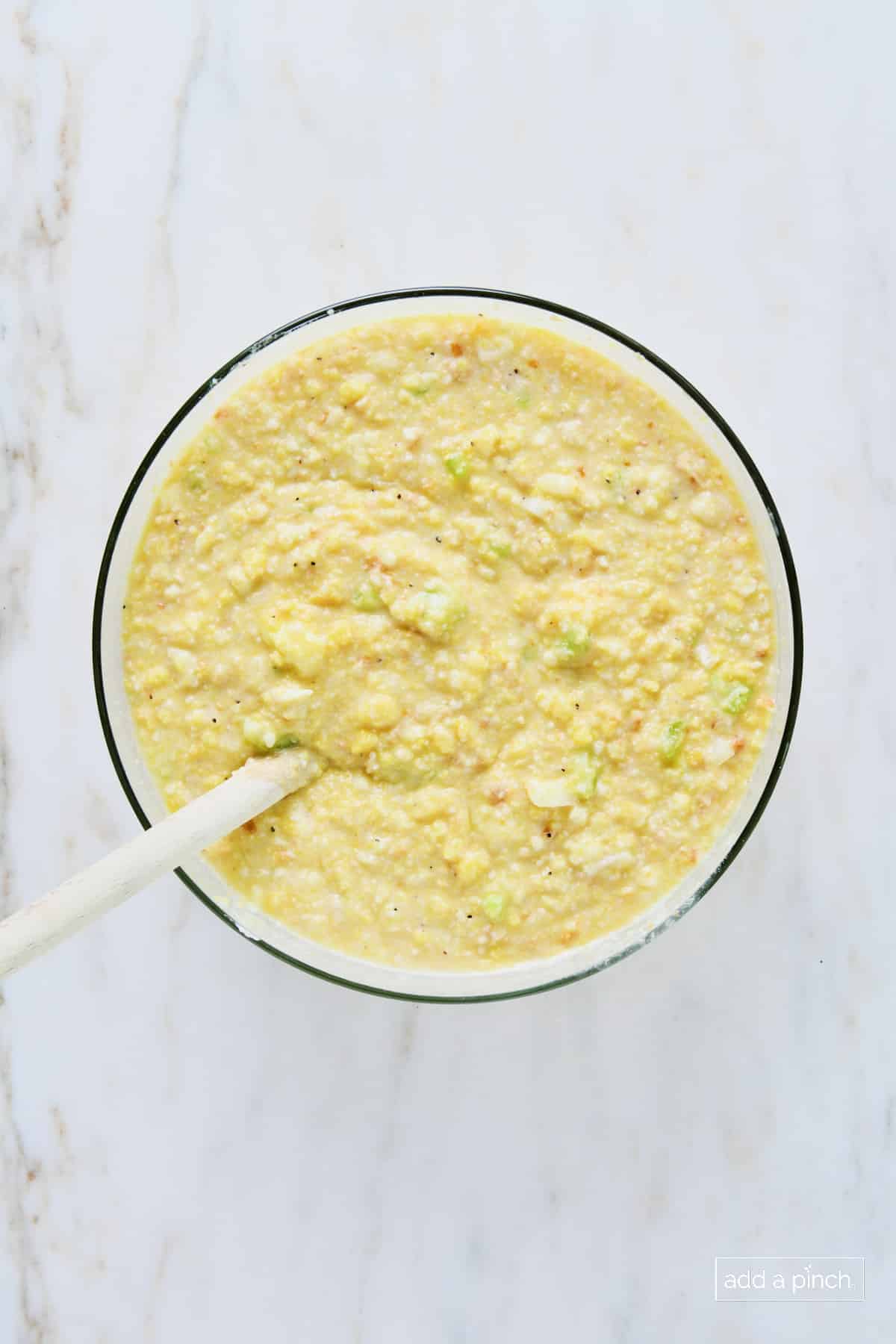 Cornbread dressing mixture in a glass bowl with a wooden spoon.