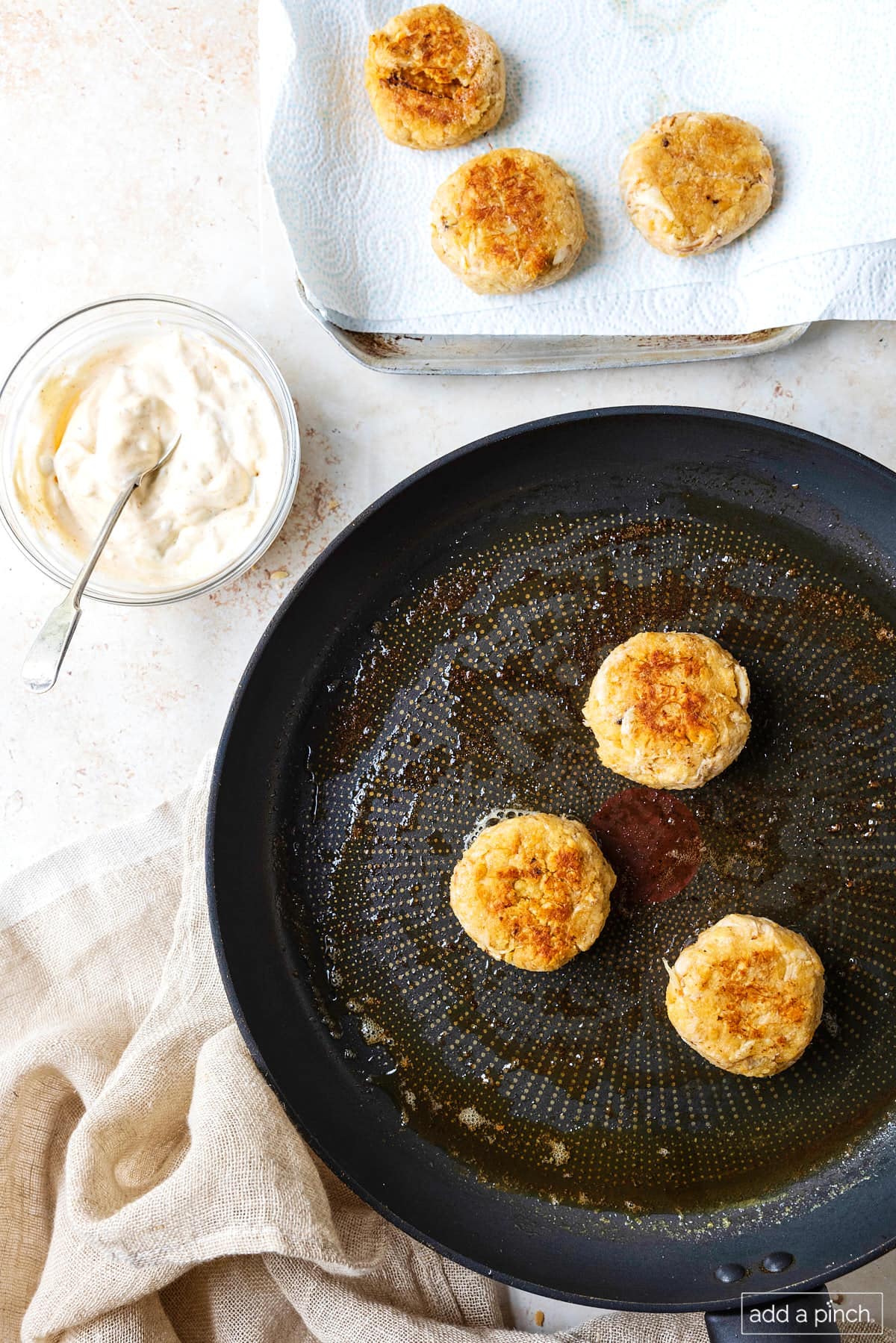 Skillet with crab cakes being cooked with some on baking sheet beside them.