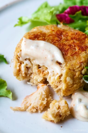 Lump crab meat shows in a golden brown crab cake on plate with salad.
