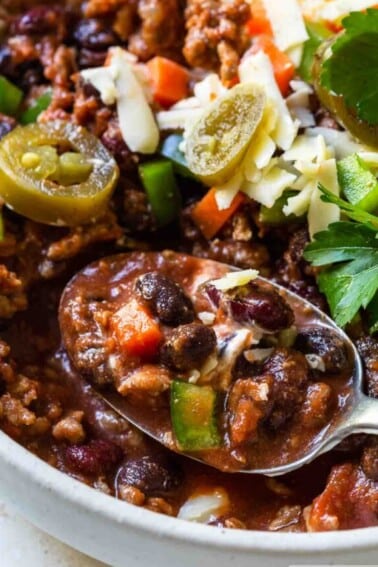 Classic chili with jalapeño, onion, grated cheese and sour cream topping. A large spoonful in a white bowl.