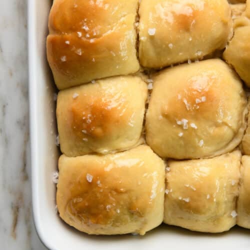 Photo of buttery dinner rolls in a white baking dish on a marble counter.