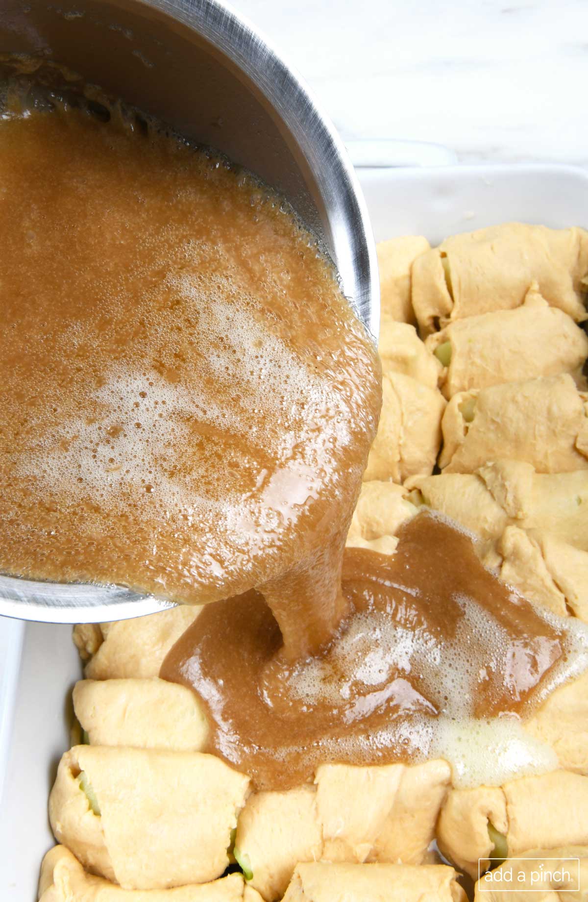 Photo of homemade caramel sauce being poured over top of apples wrapped in crescent rolls.