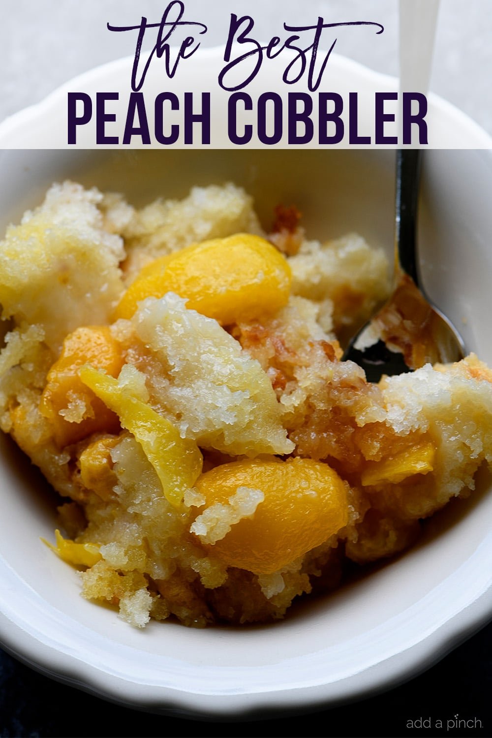 Bowl of Easy Peach Cobbler with spoon - with text - addapinch.com