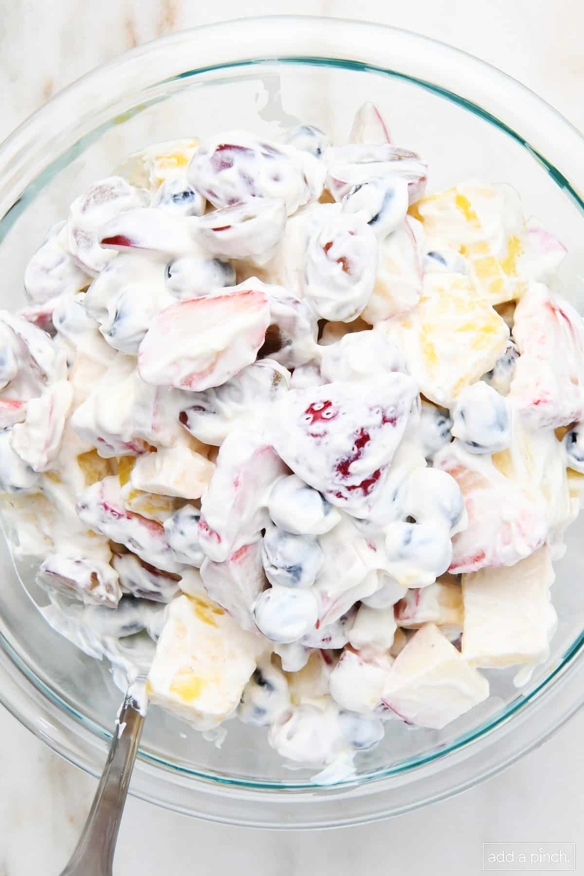 Fruit salad mixed together with a dressing in a glass bowl.