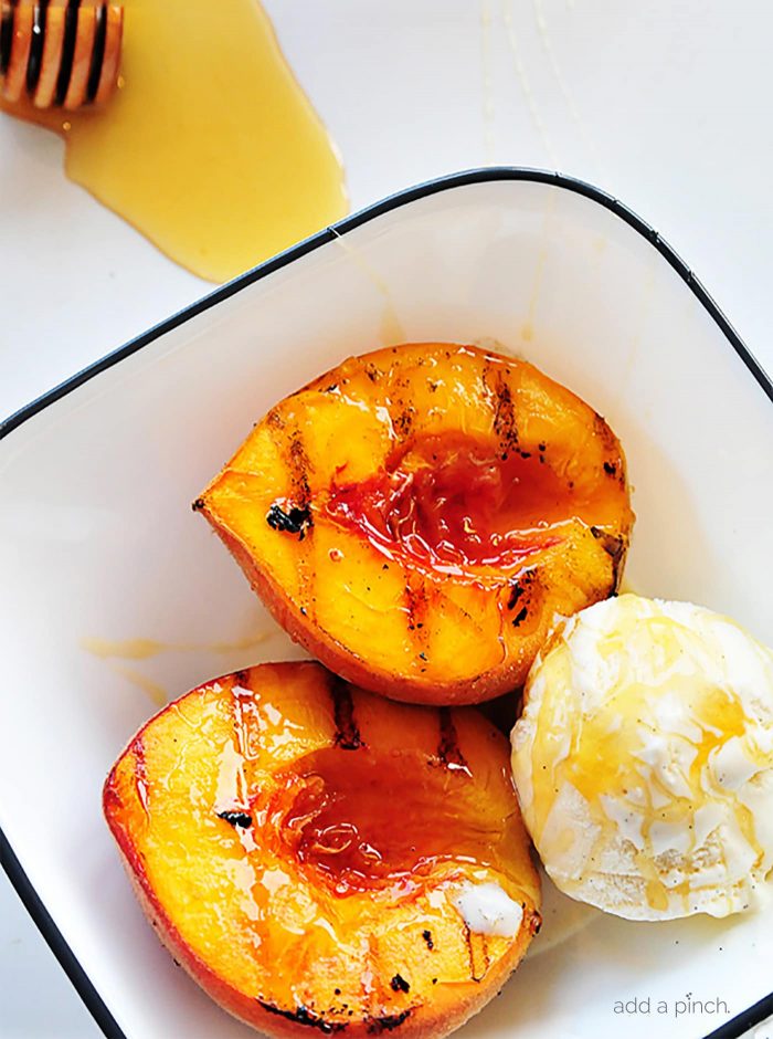 Grilled peaches with vanilla ice cream and honey in black-rimmed enamel bowl with honey on countertop // addapinch.com