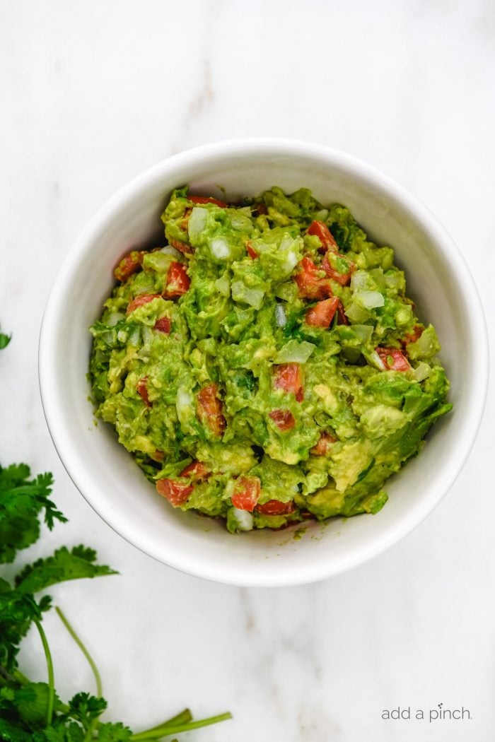 White bowl with fresh guacamole, containing tomatoes, cilantro, chopped onion and more. 