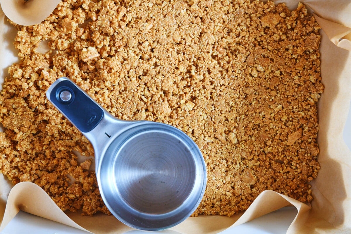 Step 3: Pressing the ingredients for the crust for the cookie bars into the baking dish with a measuring scoop.