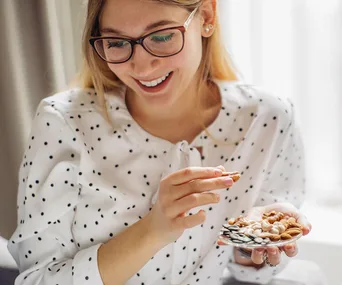 Woman smiling while holding a plate with a mix of nuts and seeds.