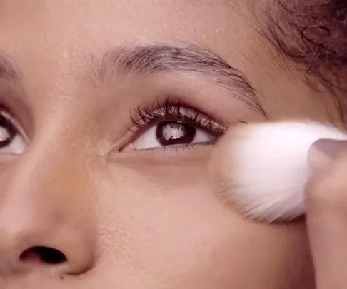 A close-up of an eye, with a makeup brush applying translucent powder to the face.