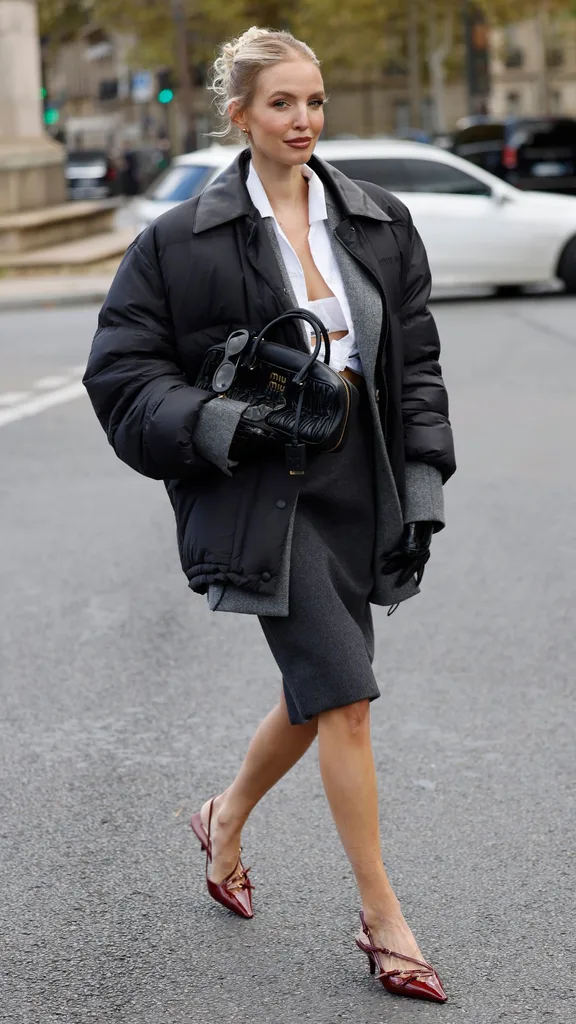 Leonie Hanne wears white Miu Miu bralette, white shirt, grey blazer, black bomber jacket, grey midi skirt, black leather gloves, black Miu Miu bag, burgundy Miu Miu heels, outside Miu Miu, during Womenswear Spring/Summer 2025 as part of Paris Fashion Week on October 01, 2024 in Paris, France.