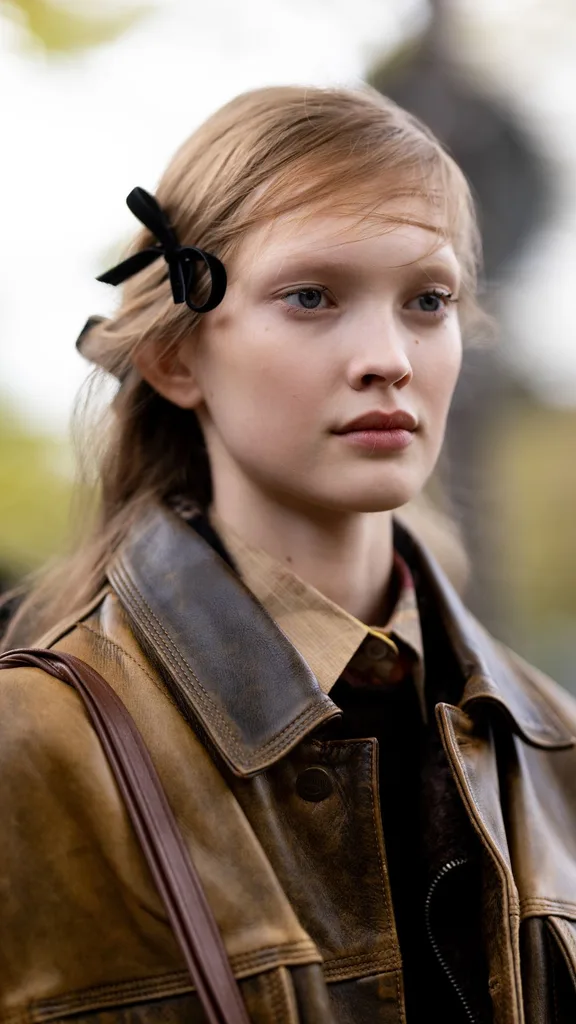 A guest wears a black velvet bow hair accessor, a beige shirt, a brown leather bag and a brown leather cargo jacket outside Valentino show during Womenswear Spring/Summer 2025 as part of Paris Fashion Week on September 29, 2024 in Paris, France. 