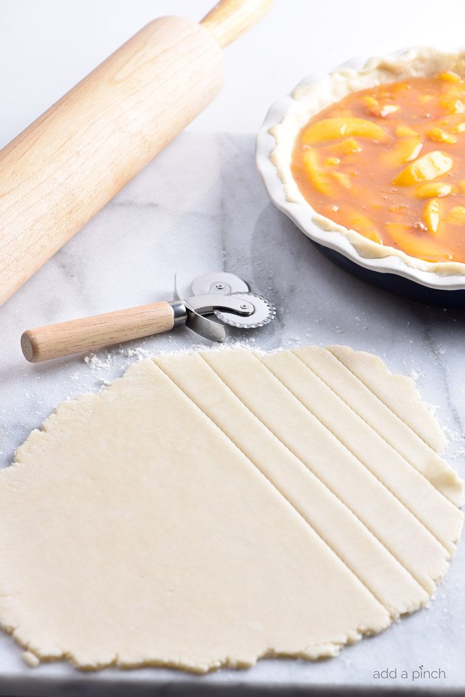 Pie crust dough on a marble surface with strips being cut to form a lattice top.