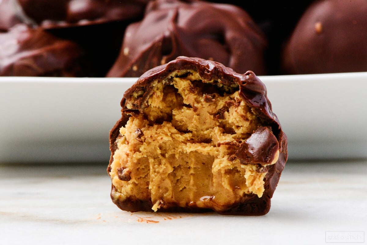 Chocolate covered peanut butter ball on a marble counter with platter filled in the background.