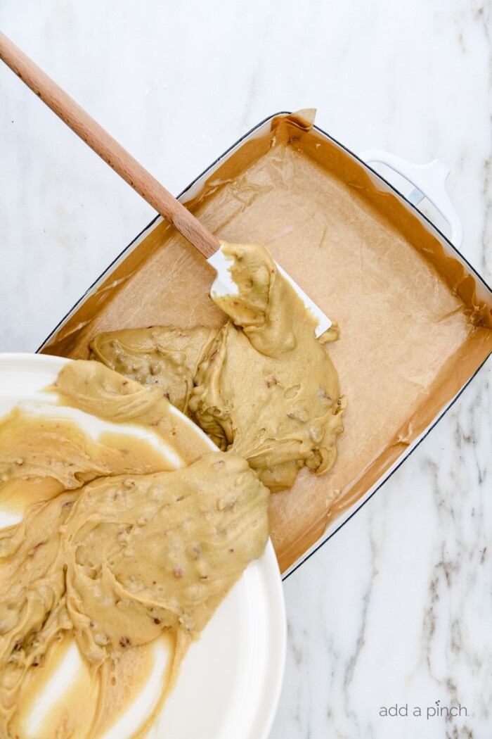 Pecan Chewies batter being poured and spread into a parchment-lined baking dish // addapinch.com