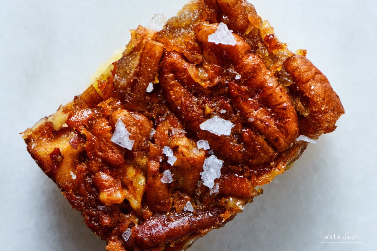 Pecan pie bar with flaky sea salt sprinkled on top on a marble counter.