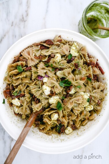 Pesto Caprese Pasta Salad Recipe - A classic pasta updated with a bright pesto dressing, sundried tomatoes, and bacon. A perfect quick and easy side dish! // addapinch.com