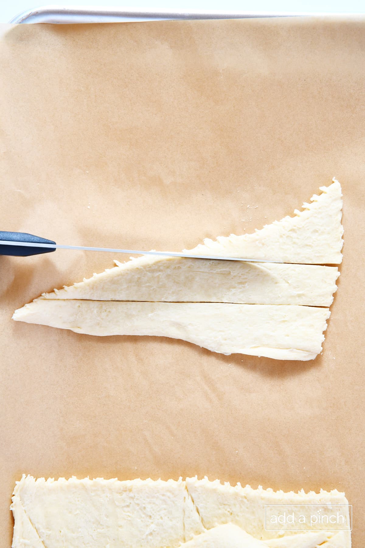 Crescent rolls on a baking sheet being cut into smaller triangles.