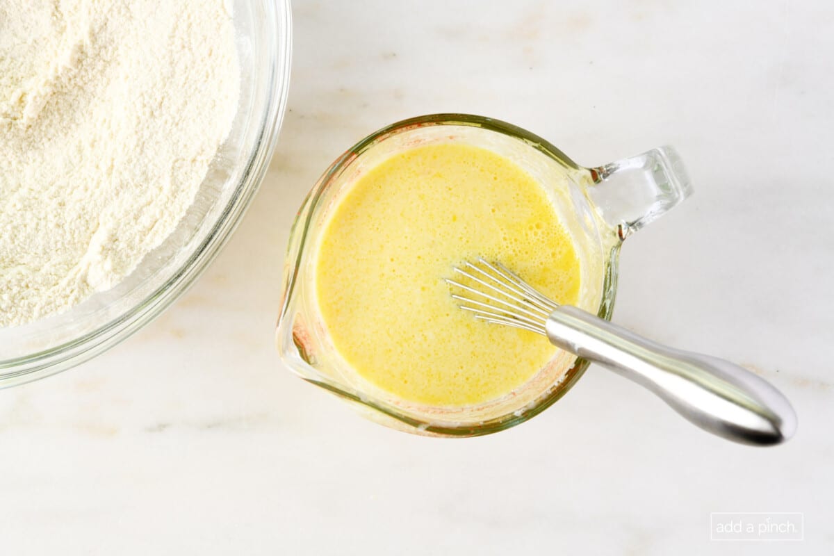 Wet ingredients whisked together in a measuring cup with a whisk on a marble surface.