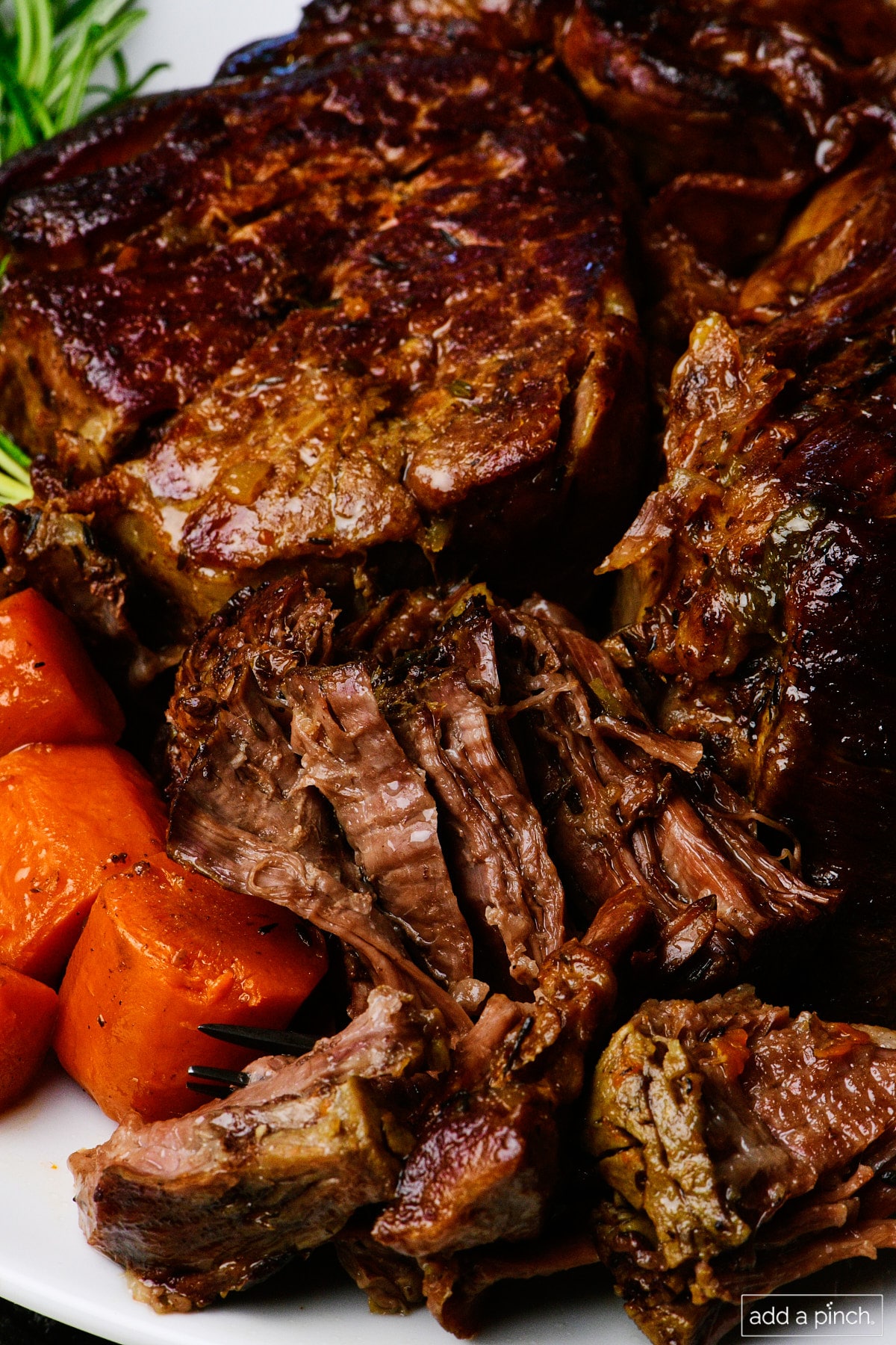 Pot roast surrounded by fresh vegetables and herbs.